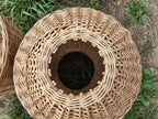 Top-down view of the wicker propane tank sleeve, its flared rim framing a hollow centre above thick walls worked in a repeating chevron willow weave.