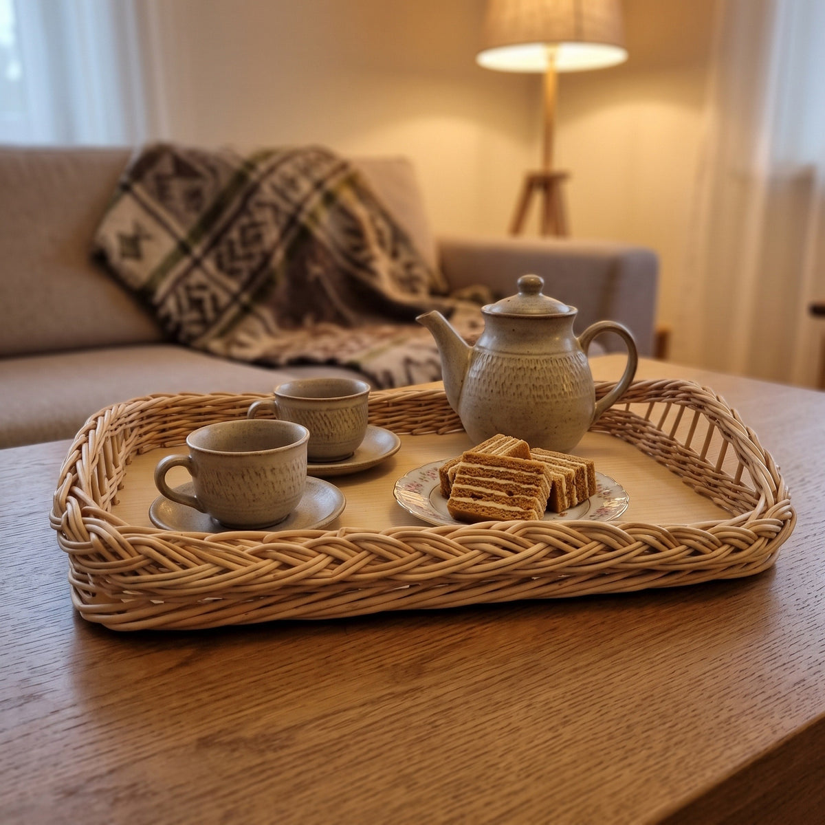 Large wicker ottoman tray with braided rim holding a teapot, cups and wafer cakes on a coffee table in a cosy living room