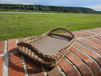 Large willow serving tray with wooden base and braided rim on a brick wall outdoors, with a green field in the background