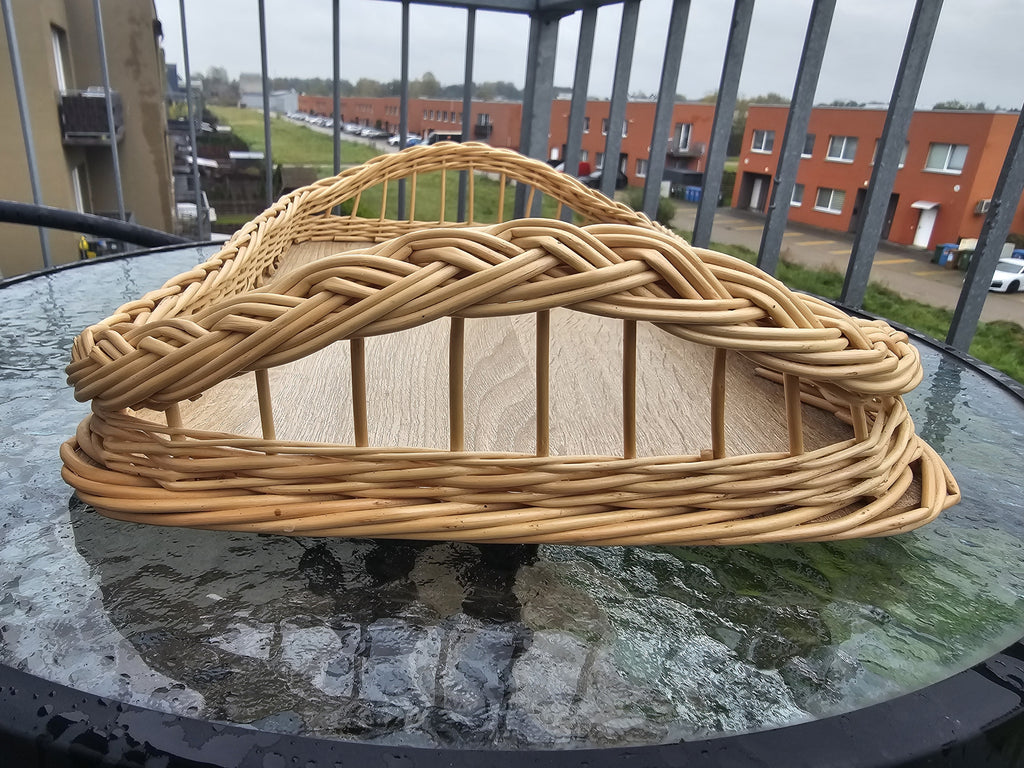 Close-up of the raised end of the handwoven wicker tray, showing the hand-braided rim over open willow spokes, on a glass table