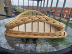Close-up of the raised end of the handwoven wicker tray, showing the hand-braided rim over open willow spokes, on a glass table