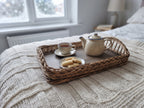 Wicker breakfast in bed tray with braided rim holding a teapot, a cup of tea and biscuits on a knitted blanket in a bedroom