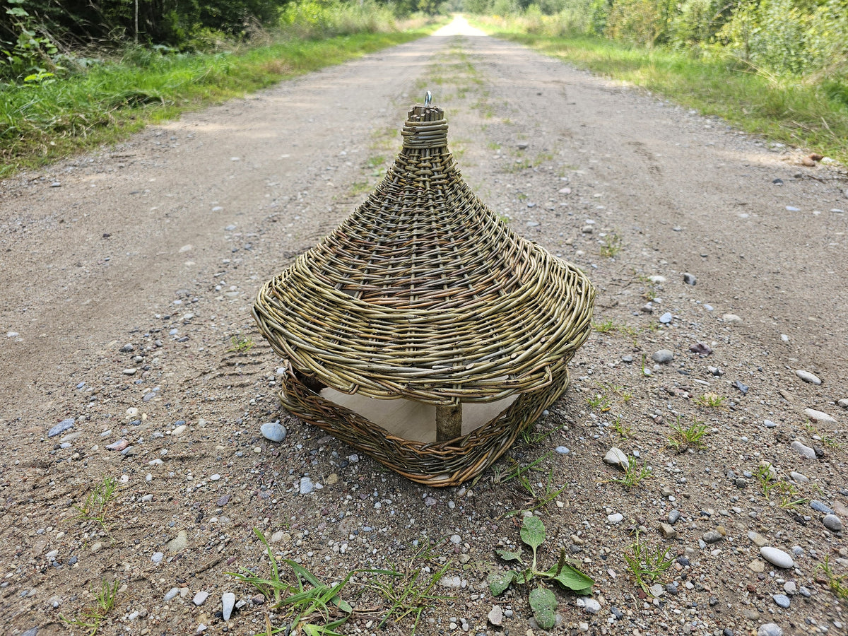 Handwoven bird feeder seen down a gravel country track, the woven roof catching the light.