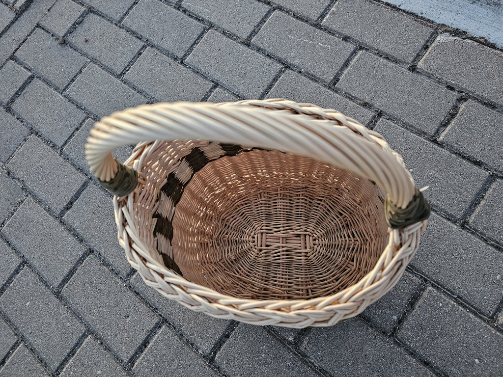 Top view of the tall willow storage basket on paving stones, showing the woven oval base, braided rim and arched handle