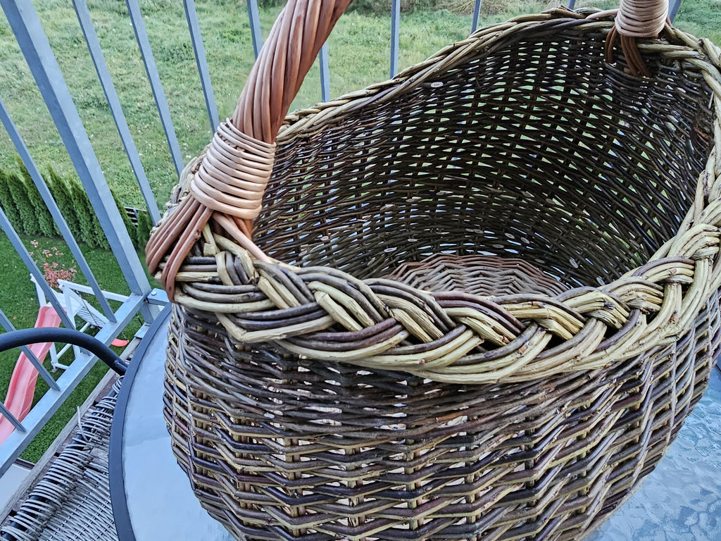 Inside view of the deep oval willow basket on a balcony table, showing the open weave, braided rim and the handle bound into the side.