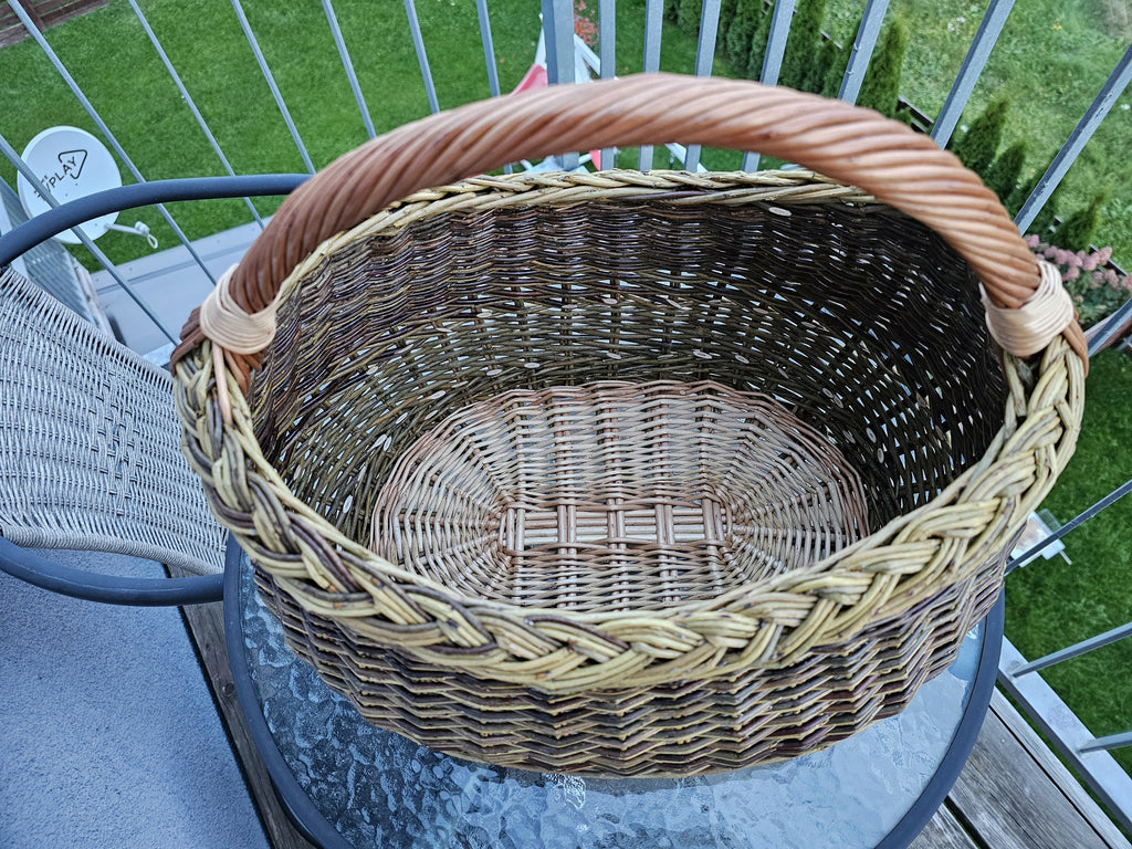 Top view into the deep oval foraging basket, showing the flat woven base with its centre slath, the braided rim and the arched handle.
