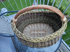 Top view into the deep oval foraging basket, showing the flat woven base with its centre slath, the braided rim and the arched handle.