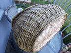 Deep wicker foraging basket lying on its side on a glass balcony table, showing the rounded belly and the woven base from below.
