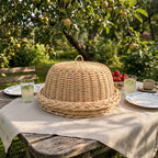 Wicker food dome on its round tray on a garden table under an apple tree, set for lunch with lemonade, strawberries and plates