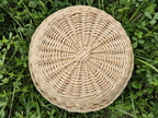 Round willow serving tray seen from above, its interlaced rods radiating outward from the flat circular base to a tightly finished rim.