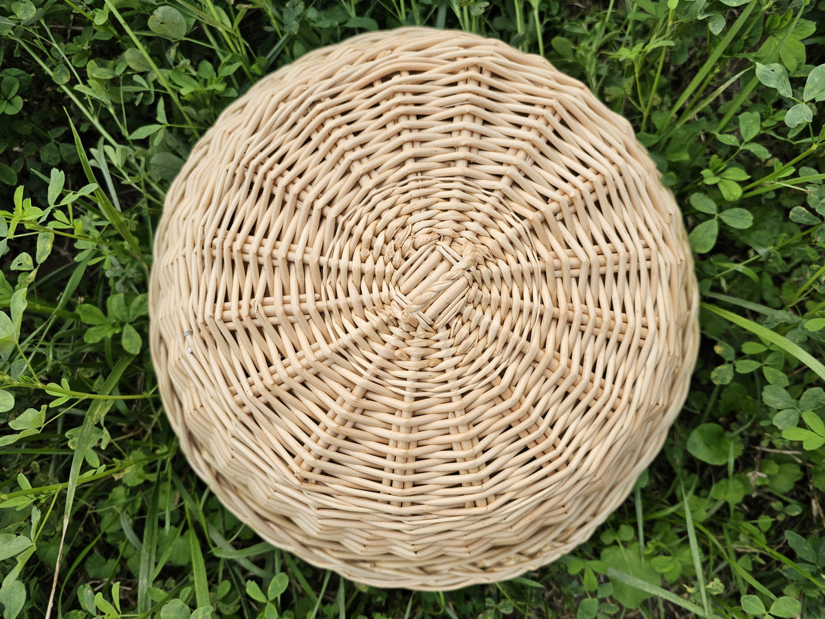 Round willow serving tray seen from above, its interlaced rods radiating outward from the flat circular base to a tightly finished rim.