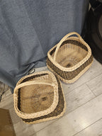 Overhead view of two handmade willow gathering baskets on a wooden floor, comparing their sizes and the radiating base weave inside each one.
