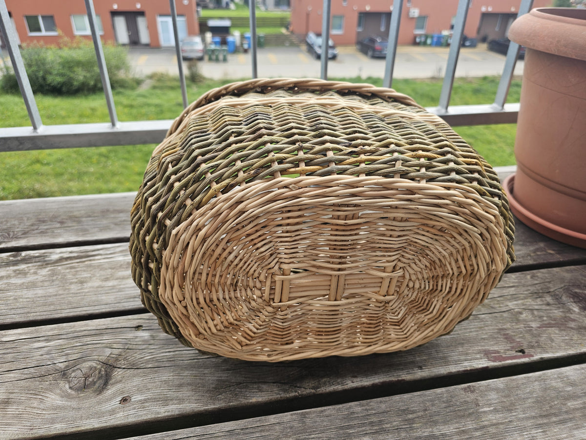 Underside of the oval handwoven wicker basket showing the sturdy woven oval base, photographed upside down on a wooden balcony table.