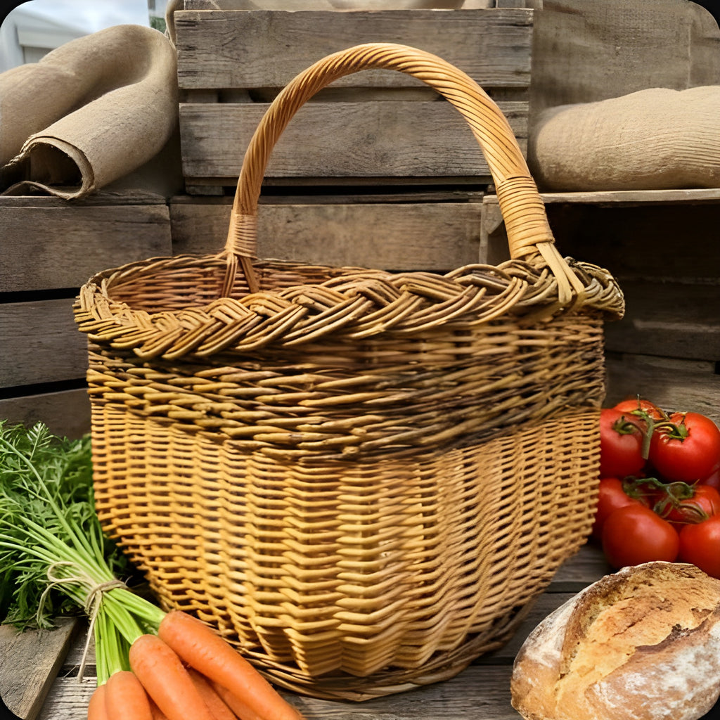Garden harvest basket with tall handle among carrots, tomatoes and a loaf of bread in front of rustic wooden crates