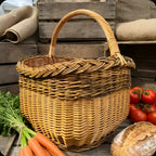 Garden harvest basket with tall handle among carrots, tomatoes and a loaf of bread in front of rustic wooden crates
