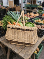 Willow garden basket with two handles filled with leeks, carrots and cabbage on a wooden stall at a farmers market.