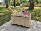 Garden basket with two crossed handles used as a picnic basket with a baguette, lemonade bottle and checked napkin in a park.