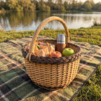 Round foraging basket with handle packed with a picnic lunch, apples and a thermos on a tartan blanket by a lake at golden hour