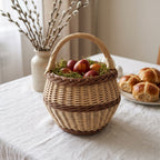 Small round wicker Easter basket with handle filled with dyed eggs on moss, on a linen table with pussy willow and hot cross buns