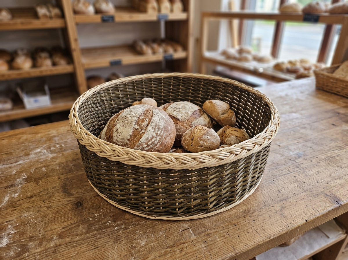 Wide low handwoven willow basket with a braided rim filled with sourdough loaves and rolls on a wooden bakery table