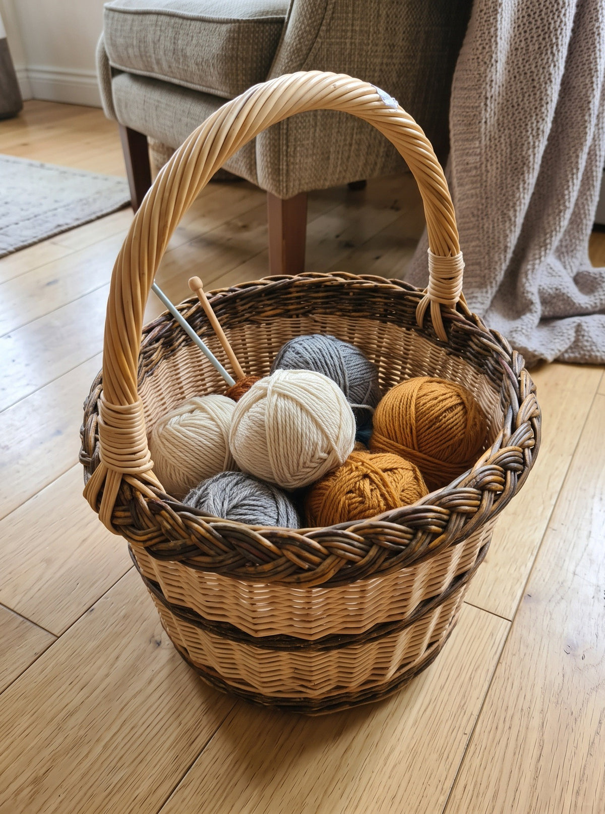Round wicker basket with handle used as a knitting basket for balls of yarn and needles on a wooden floor by an armchair