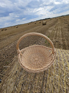 Empty round willow harvest trug on a hay bale, with more bales scattered across the stubble field under a cloudy sky.