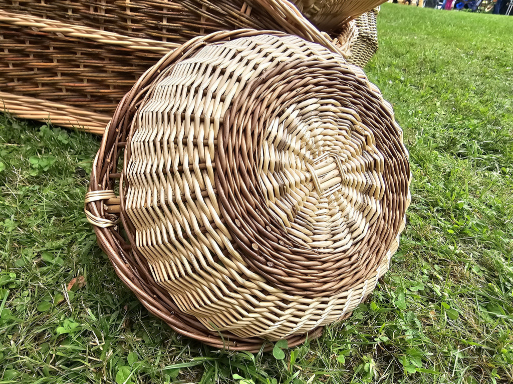 Round willow garden trug resting on its side in the grass, showing the full circular base weave and sturdy braided edge