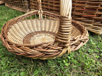 Round willow garden trug on the grass showing the woven base inside its thick braided rim, with other wicker baskets alongside