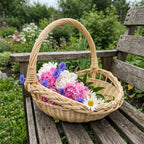 Willow harvest trug with handle filled with peonies, cornflowers and daisies on a weathered wooden garden bench