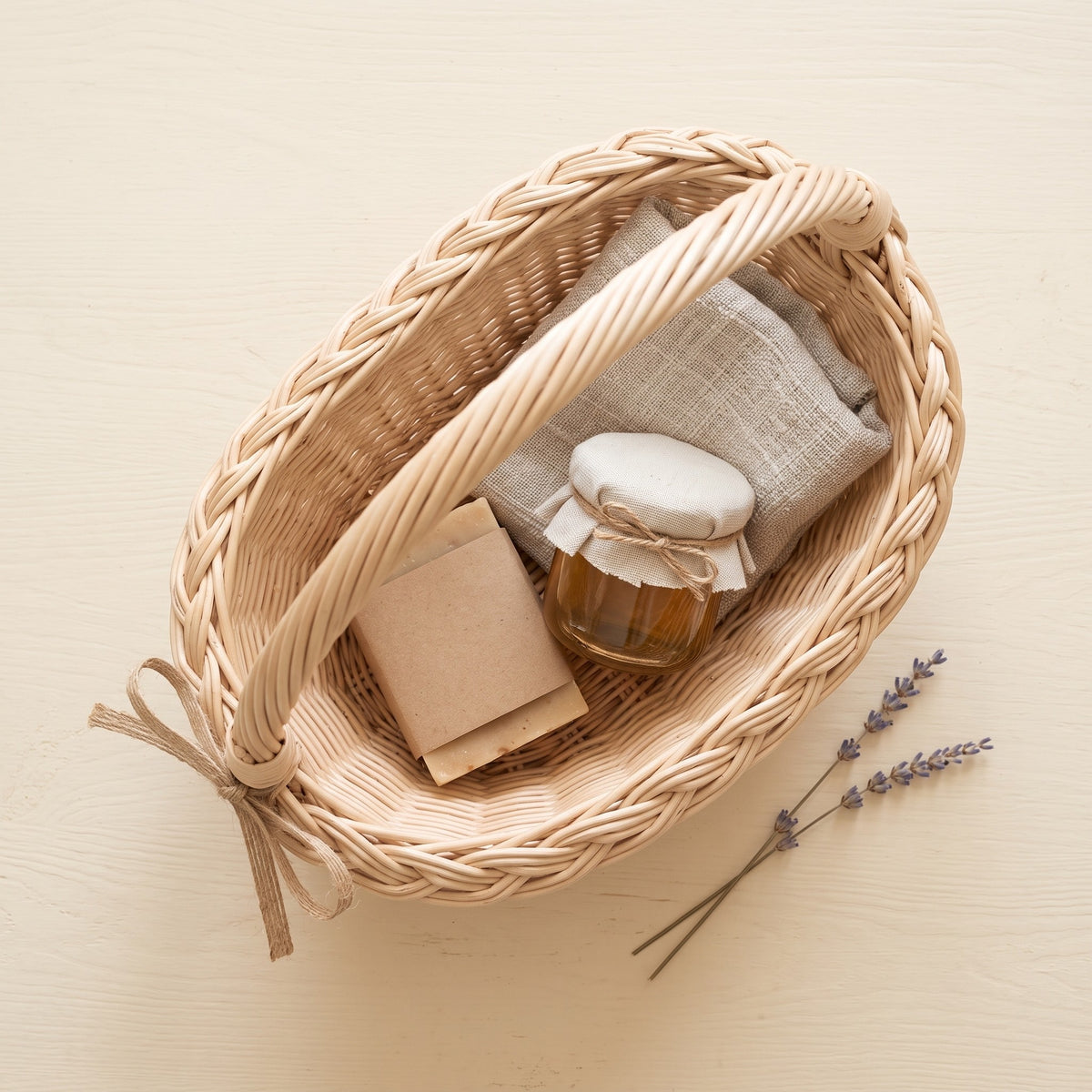 Small willow gift basket seen from above holding a wrapped soap, a jar of honey and a linen cloth, with lavender sprigs beside it