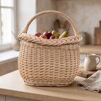 Small handwoven berry basket with curved handle filled with red apples and pears on a wooden kitchen counter by a jug
