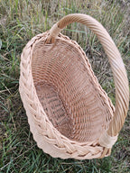 Close view into the empty willow basket in the grass, the thick plaited rim and generous curved handle showing the handmade construction.