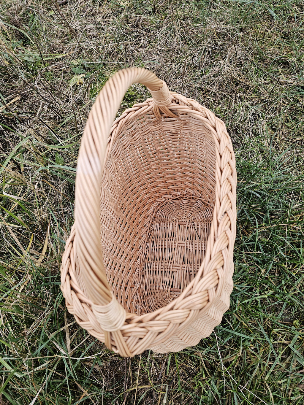 Overhead view of the oval wicker basket on grass, revealing the braided rim running right around it and the woven base panel inside.