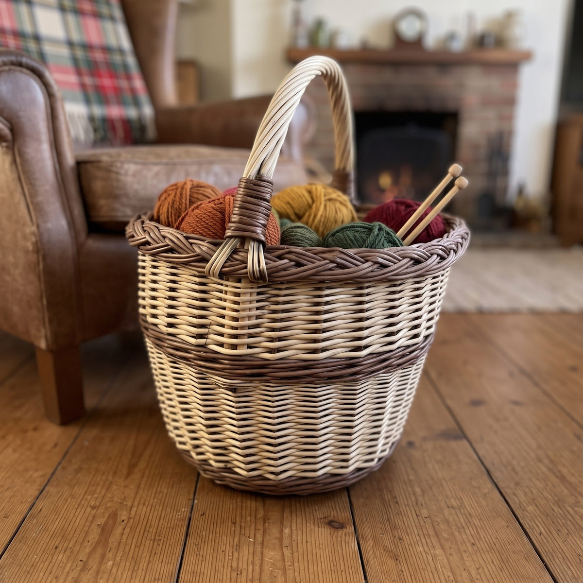 Handwoven wicker basket with handle holding balls of yarn and knitting needles on a wooden floor by an armchair and a fireplace