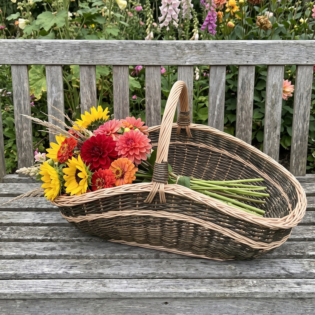 Extra large garden trug basket with a tall arched handle holding a bunch of sunflowers, dahlias and zinnias on a weathered wooden garden bench