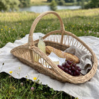 Large wicker trug with handle packed for a picnic with bread, cheese, grapes and lemonade on a linen cloth by a lake