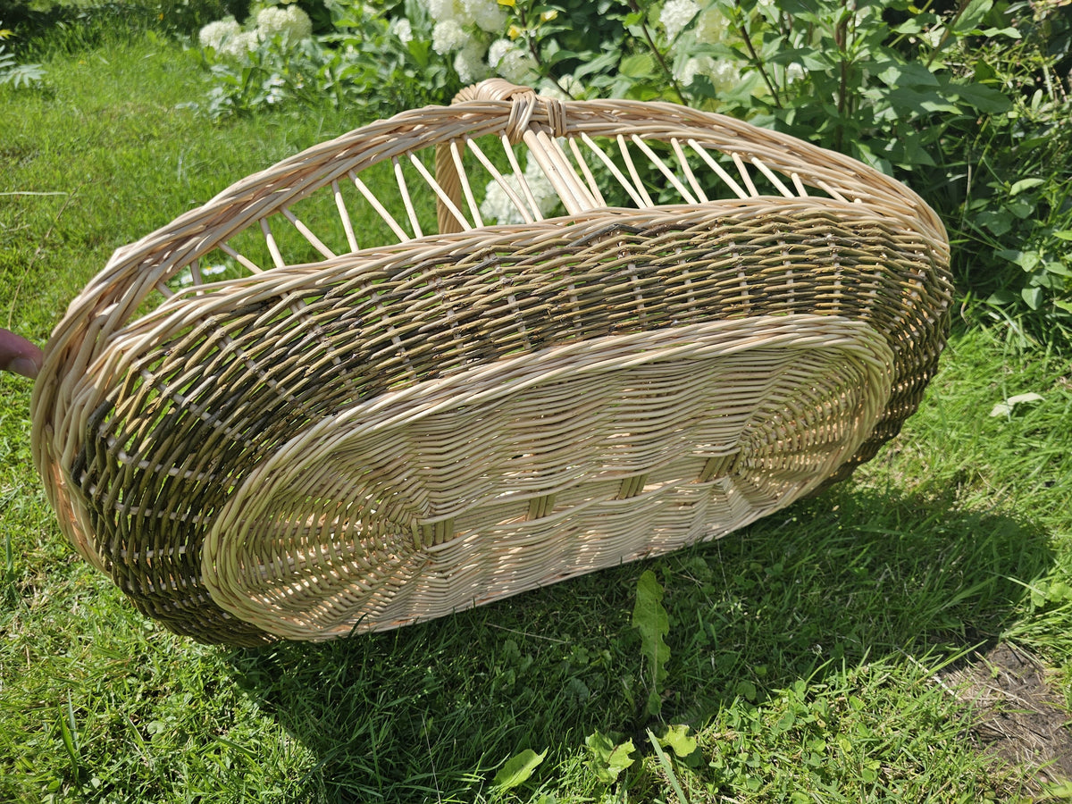 Large willow harvest trug tipped on its side on the grass to show the tightly woven oval base and the open upper section
