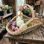 Large willow flower gathering trug with a tall handle filled with roses, hydrangeas and lavender on a potting bench in a garden shed