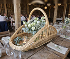 Open-weave willow trug with handle filled with white flowers and eucalyptus as a centrepiece on a rustic barn wedding table