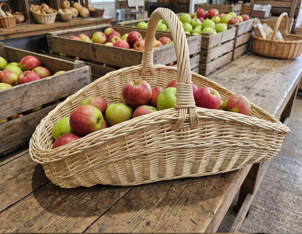 Großer Gartenkorb voller roter und grüner Äpfel auf einem rustikalen Holztisch zwischen Apfelkisten auf dem Markt