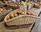 Großer Gartenkorb voller roter und grüner Äpfel auf einem rustikalen Holztisch zwischen Apfelkisten auf dem Markt