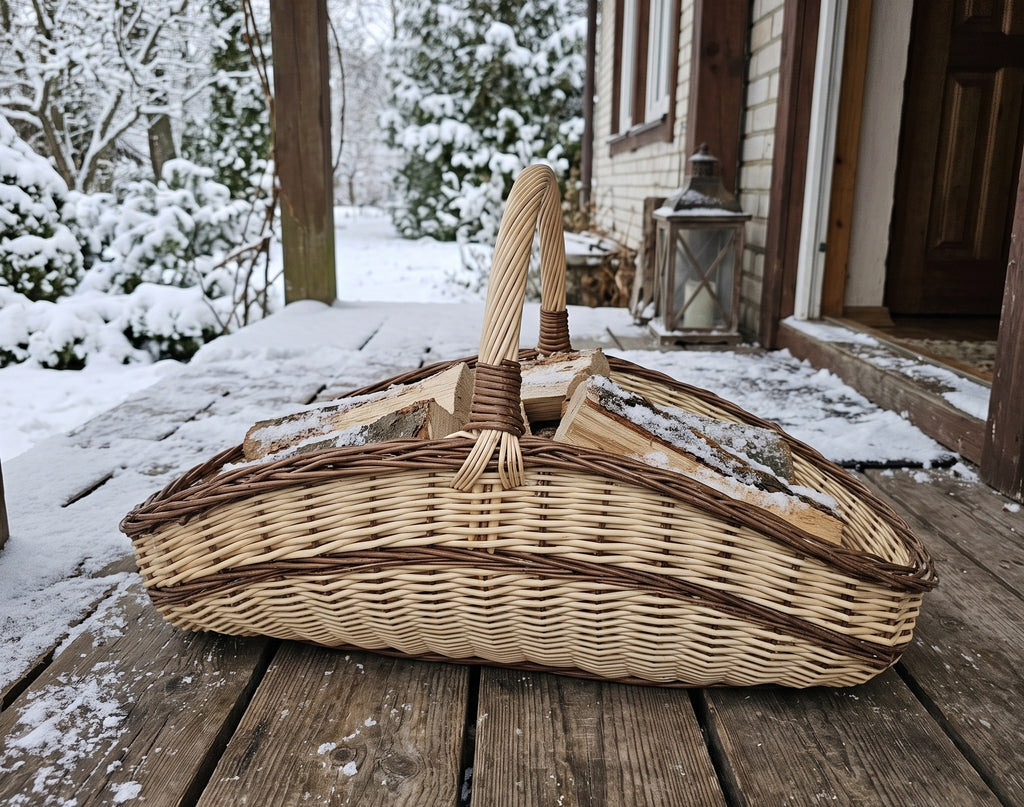Large wicker trug basket loaded with firewood on a snowy wooden porch outside a country house in winter.