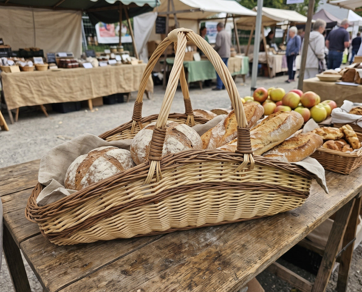 Handwoven willow market trug with two crossed handles filled with sourdough loaves and baguettes on a bakery stall at an outdoor market
