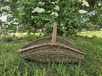 Extra large willow garden trug with handle standing on a lawn in front of a flowering elder bush.