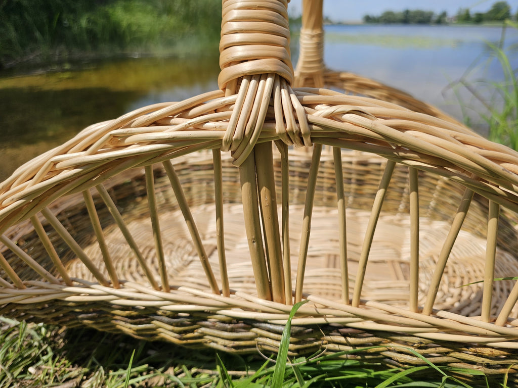 Close view of the open-rib weave of the willow trug by a lake, with thin upright rods rising from the woven base to the rim