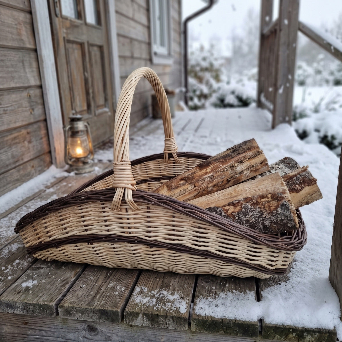 Large willow log trug with tall handle full of split logs on a snow-covered porch beside a lantern.