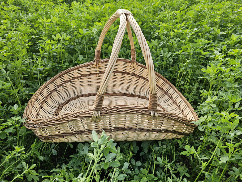 Crescent-shaped willow flower trug with a wide open top and curved base, its two handles rising from the centre among green clover