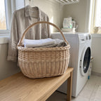Willow harvest basket with handle used for folded laundry on a wooden bench next to a washing machine