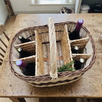 Top view of the handwoven willow wine carrier with dividers on a farmhouse table, six wine bottles in separate compartments and a rosemary sprig.