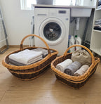 Two nesting wicker baskets with handles used as laundry room storage, holding folded towels and linen next to a washing machine